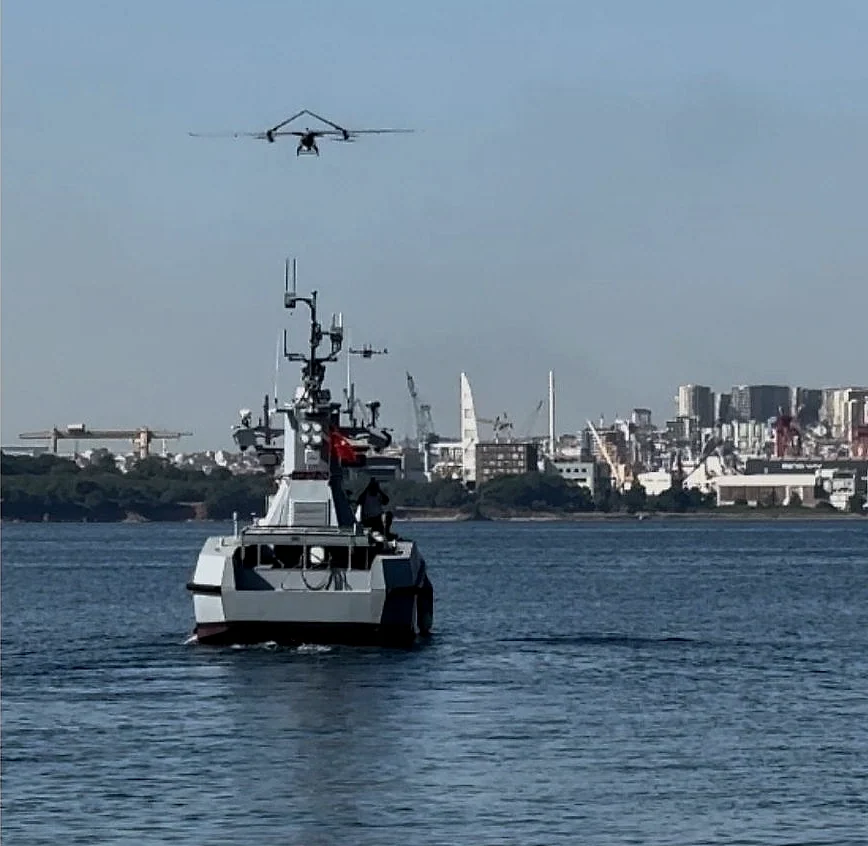 A SkyCopes VTOL aircraft flying above a naval vessel at sea during an autonomous ship landing